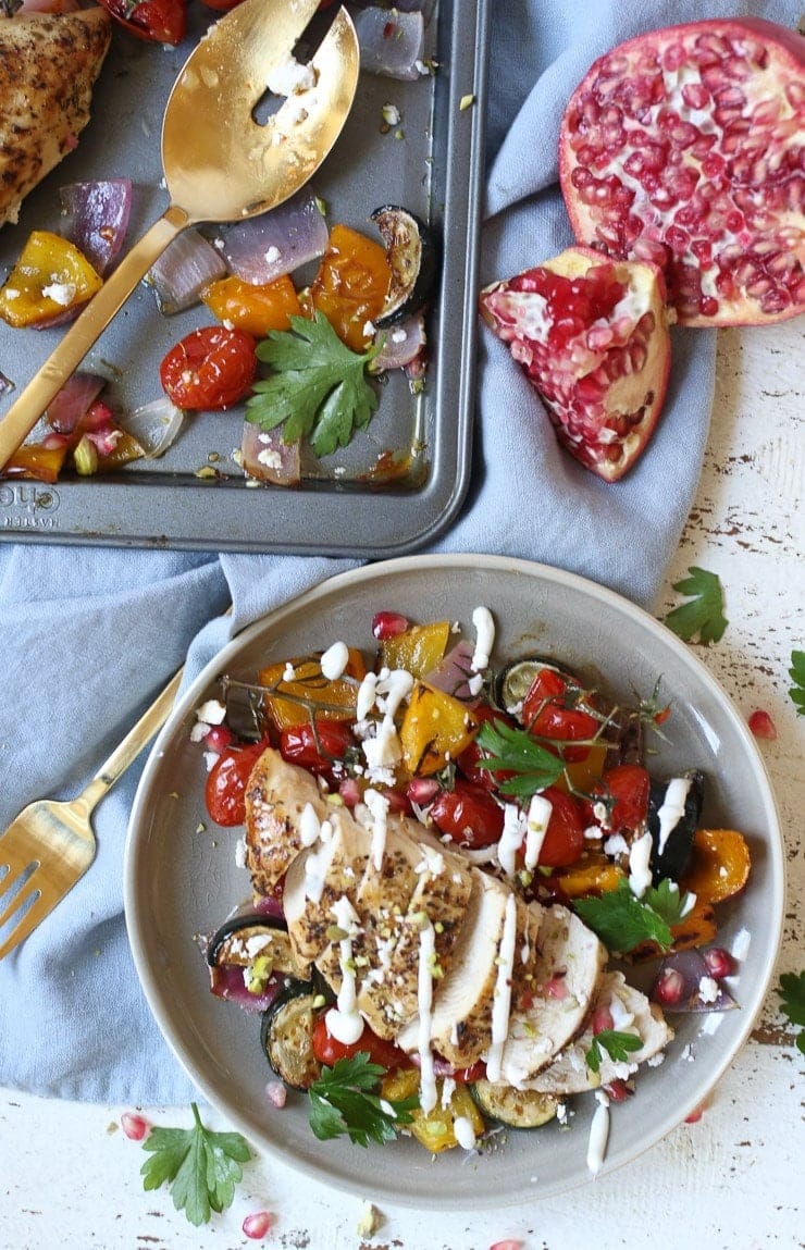greek-sheet-pan-chicken-breasts Plate with chicken cooked in a sheet pan served with sautéed vegetables on sides drizzled with white sauce.