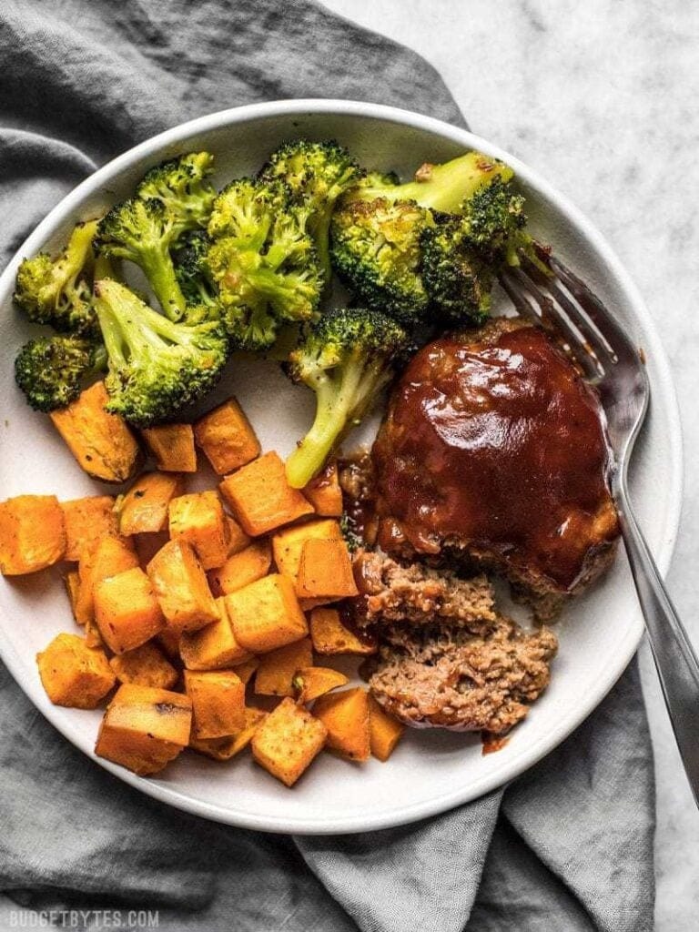 sheet-pan-bbq-meatloaf-dinner Sliced BBQ meatloaf topped with gravy served on a plate with broccoli, and roasted potatoes.