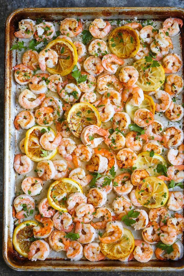 sheet-pan-garlic-butter-shrimp Buttered shrimp cooked with butter and lemon slices on a sheet pan seasoned and garnished with chopped parsley.