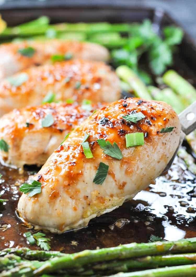 sheet-pan-honey-apricot Chicken breast and asparagus cooked in a sheet pan with with orange juice, honey, garlic, and soy sauce garnished with chopped parsley.