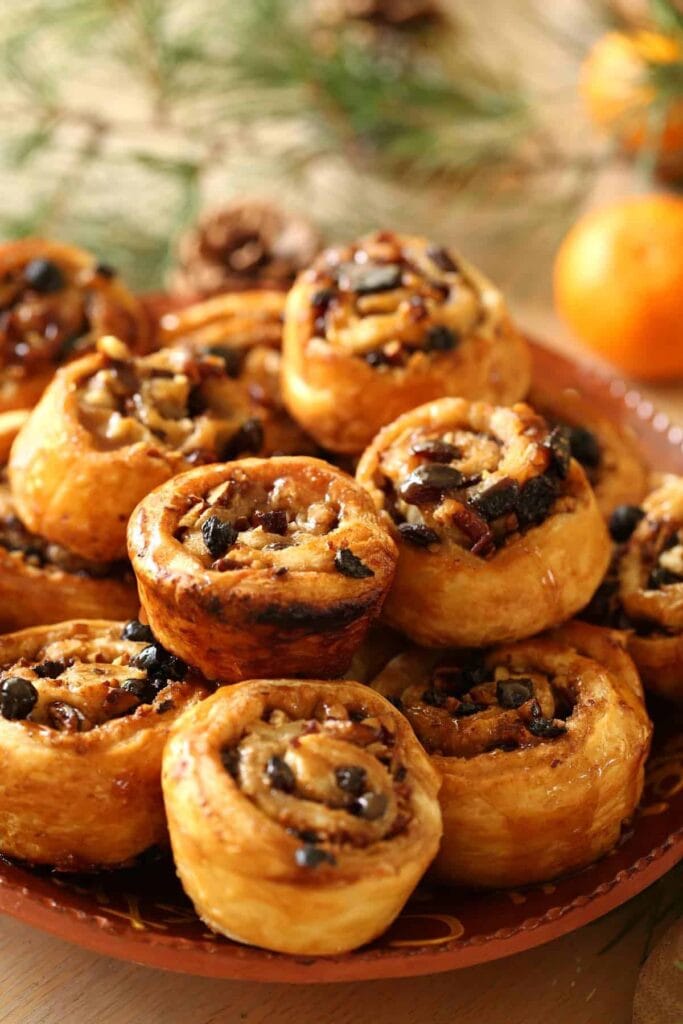 Bunch of glazed small buns with pecans and raisins on a wooden plate.
